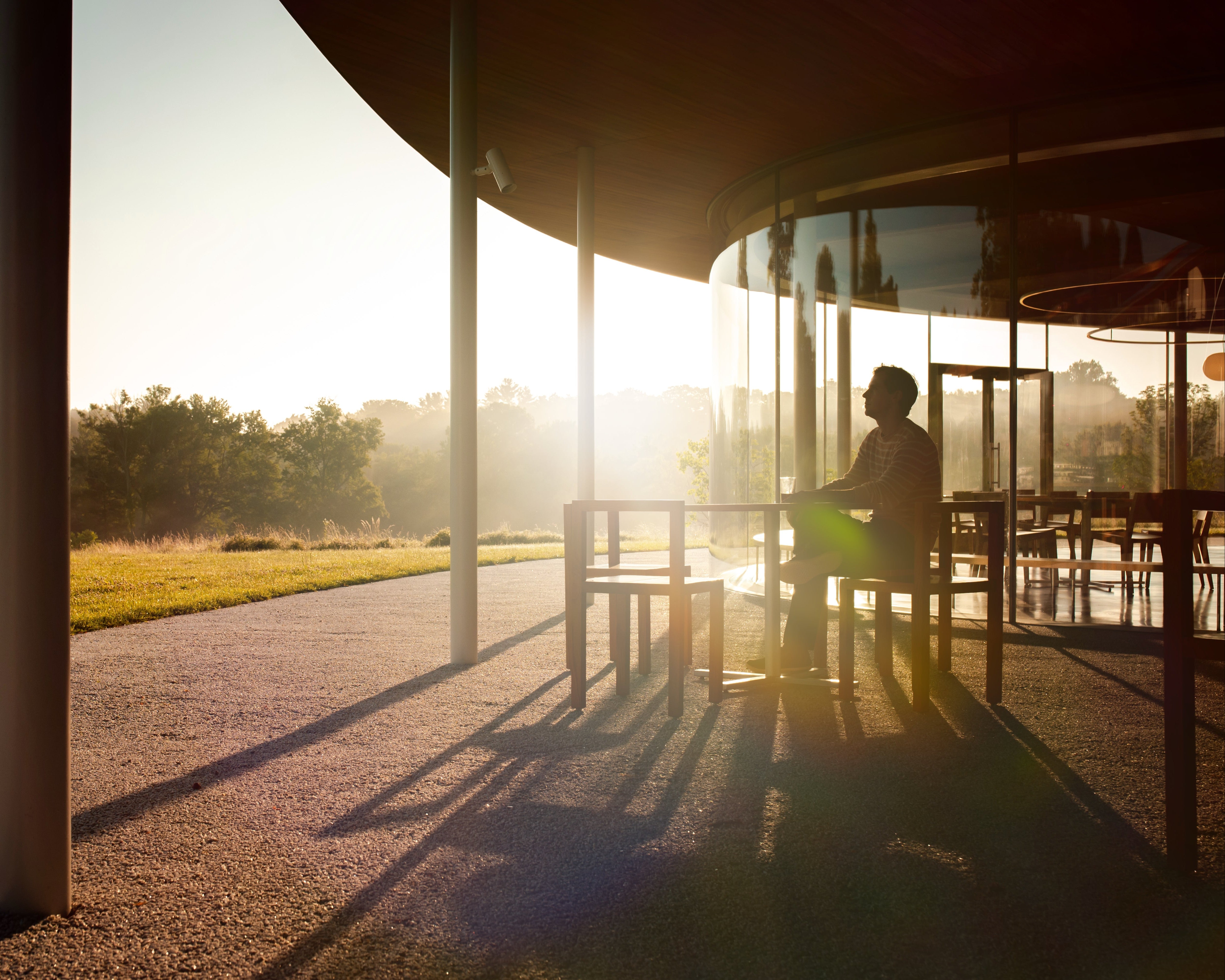 Person sitting at a table outside during sunset with trees in the background