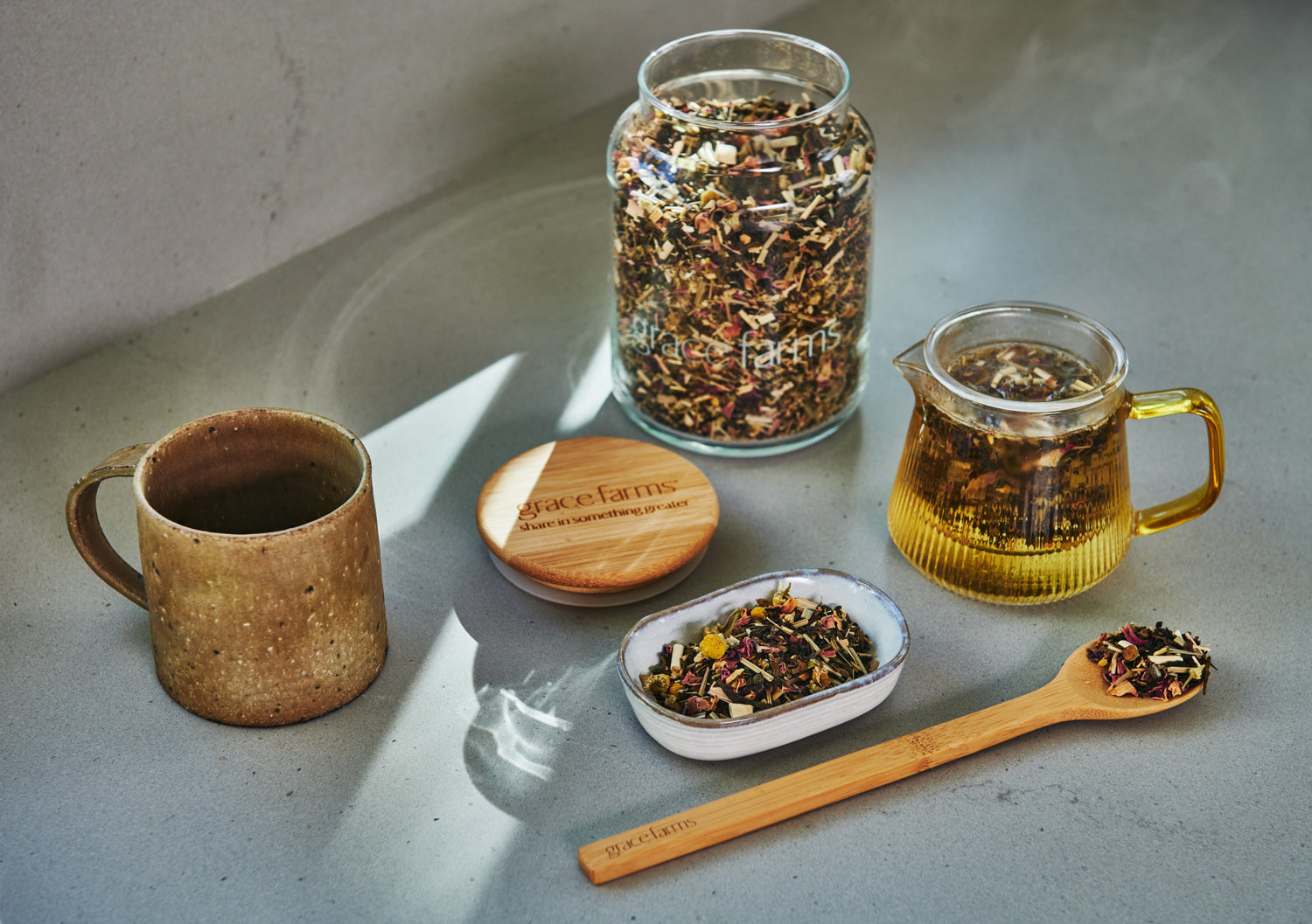 Tea-making setup with a mug, jar, teapot, and wooden spoon on a light surface.