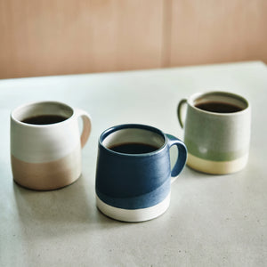 Three ceramic KINTO mugs with different color schemes on a light surface.